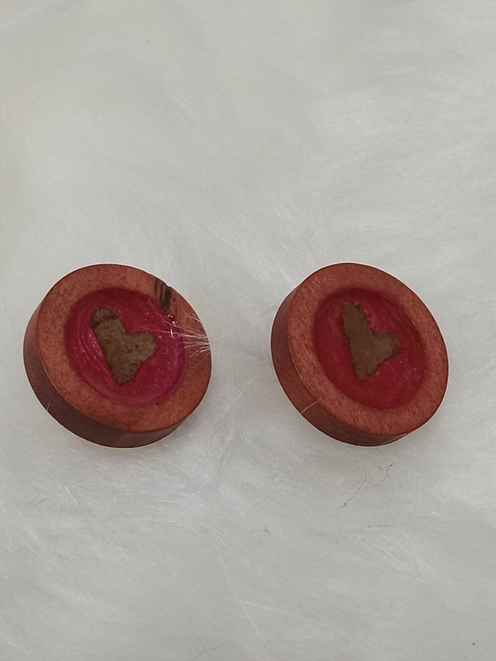 Handmade earrings on a wooden base with a piece of punched-out tree leaf